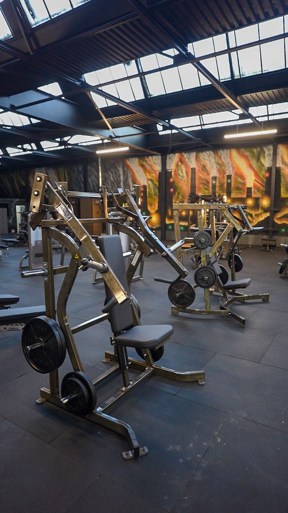 Foundry Gym Warwick strength-training floor with exposed roof structure and illuminated murals